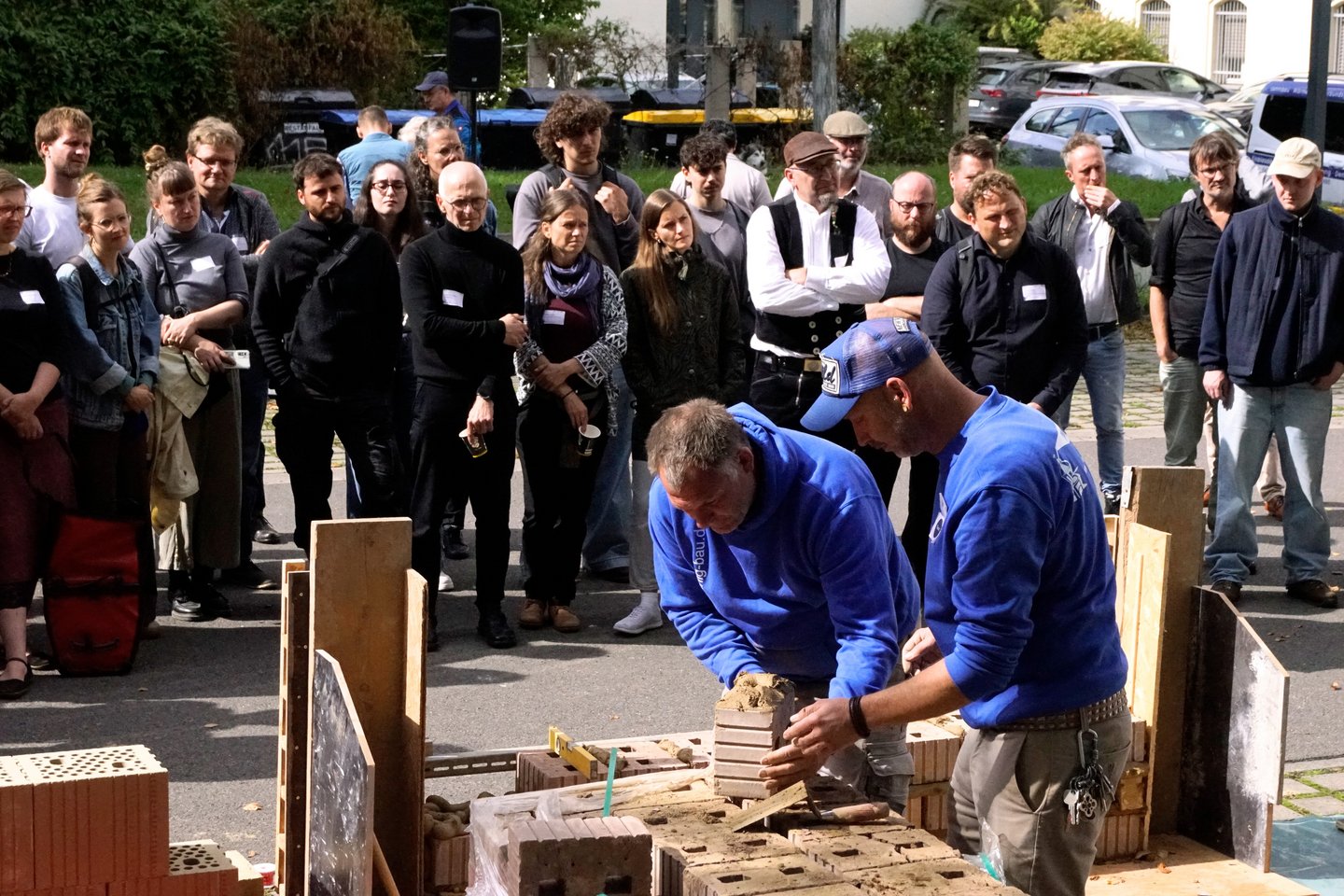 zwei Männer bauen eine Wand, viele Menschen schauen zu