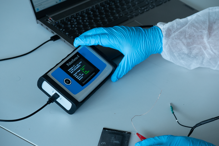 Foto von Analysegerät, kleines Gerät, dass in Hand passt und Messdaten mit Kabel an Laptop überträgt, wird mit Hand in hellblauem Gummi-Handschuh festgehalten
