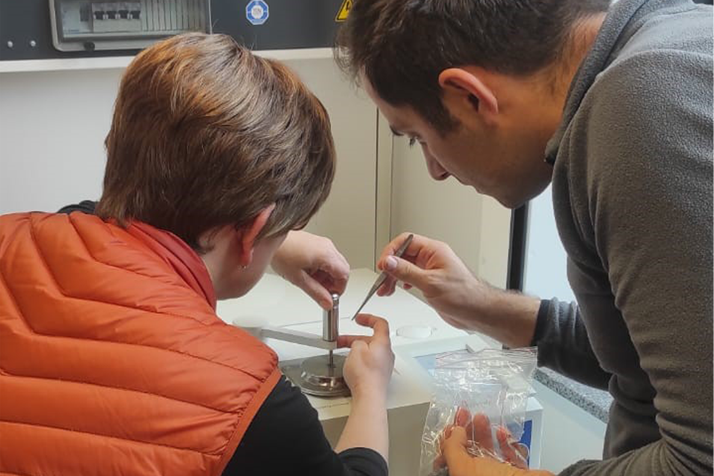 Nahaufnahme von Dr. Mustafa Zor (rechts) und Dr. Andrea Berlich (links), Personen sind von hinten zu sehen, experimentieren gerade mit kleinem Gerät