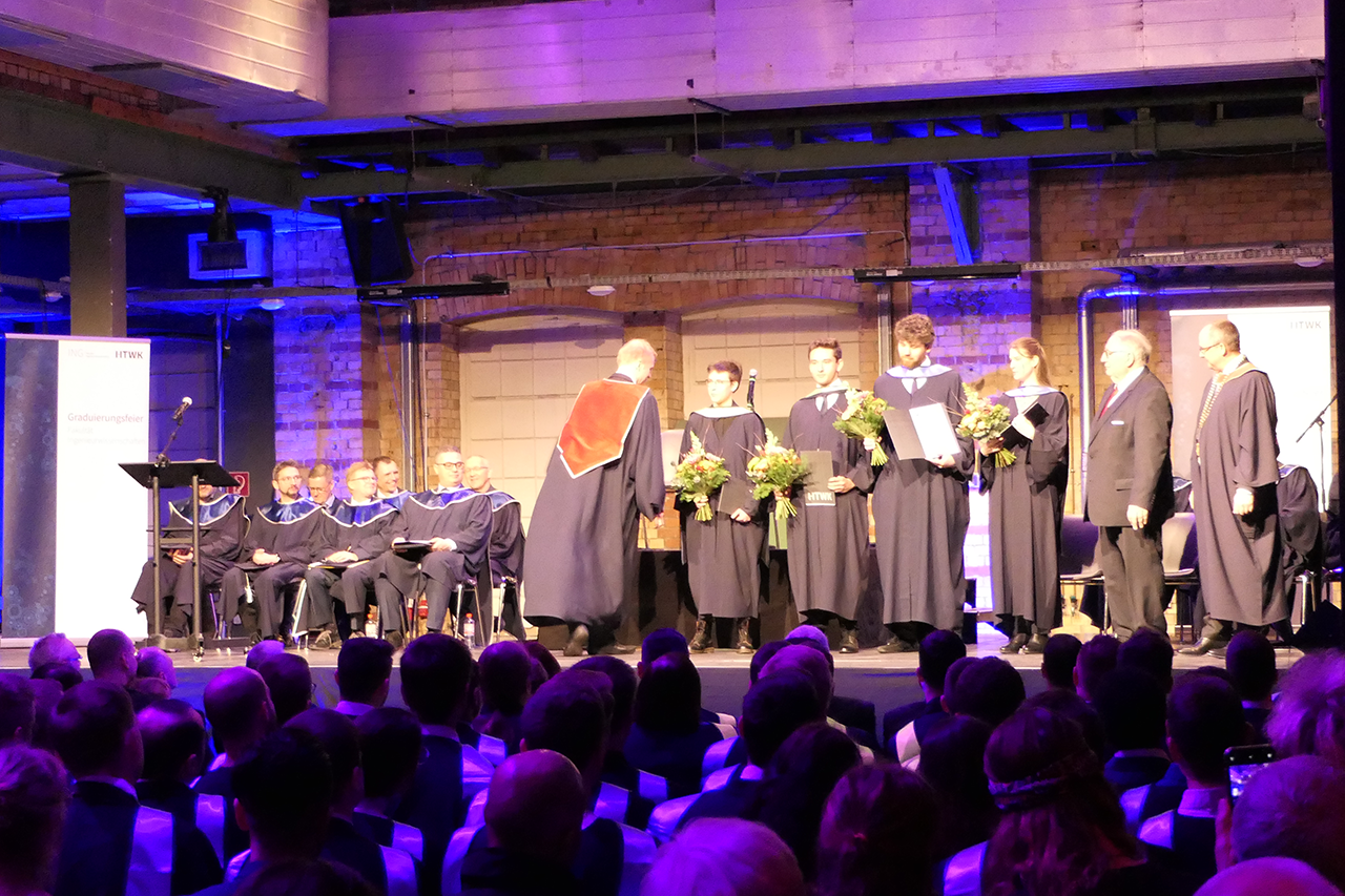 Foto von hinten nach vorne zur Bühne, wo gerade Absolvent graduiert wird